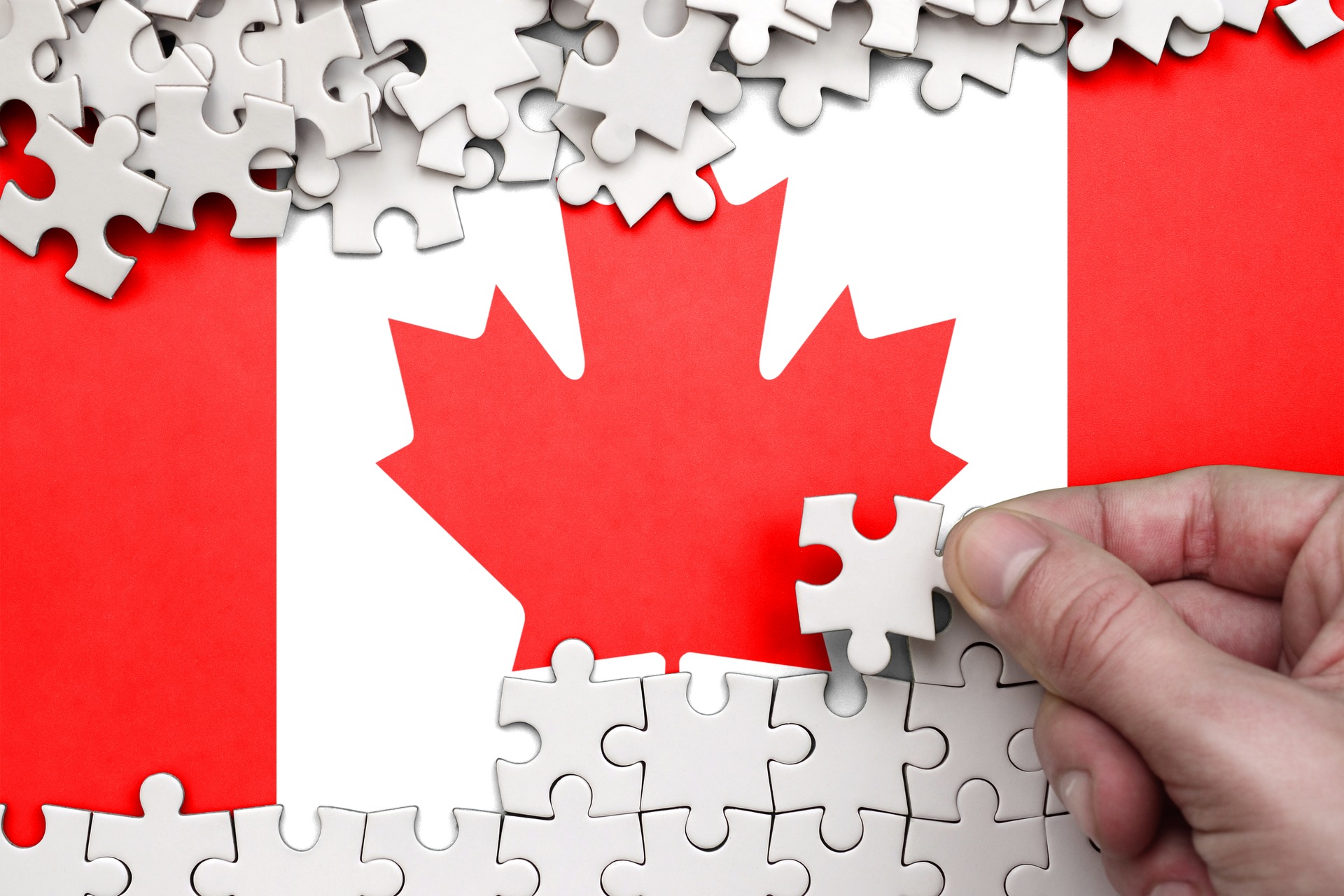 Hand placing puzzle piece on Canada flag