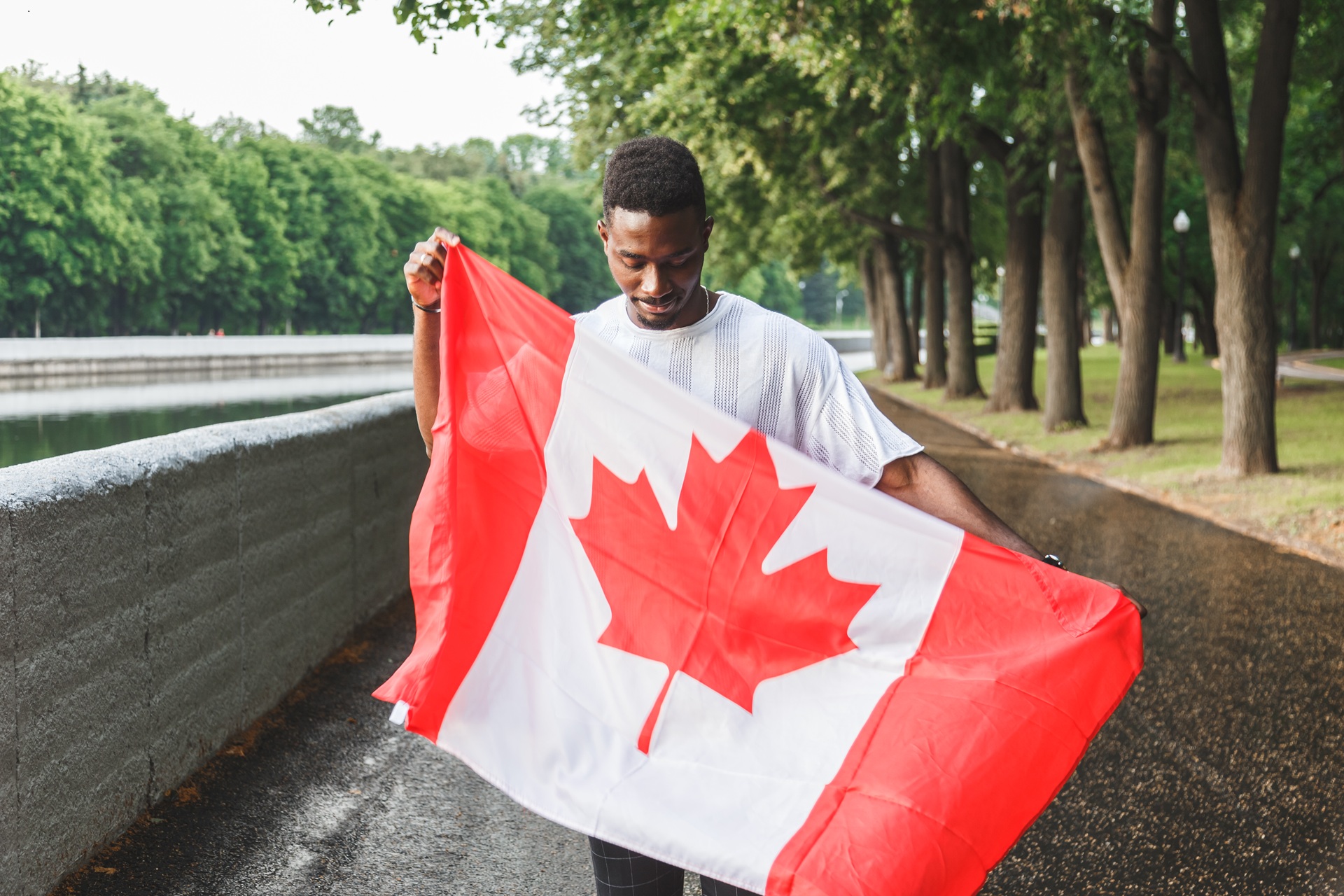 Man holding Canadian flag near riverside walkway