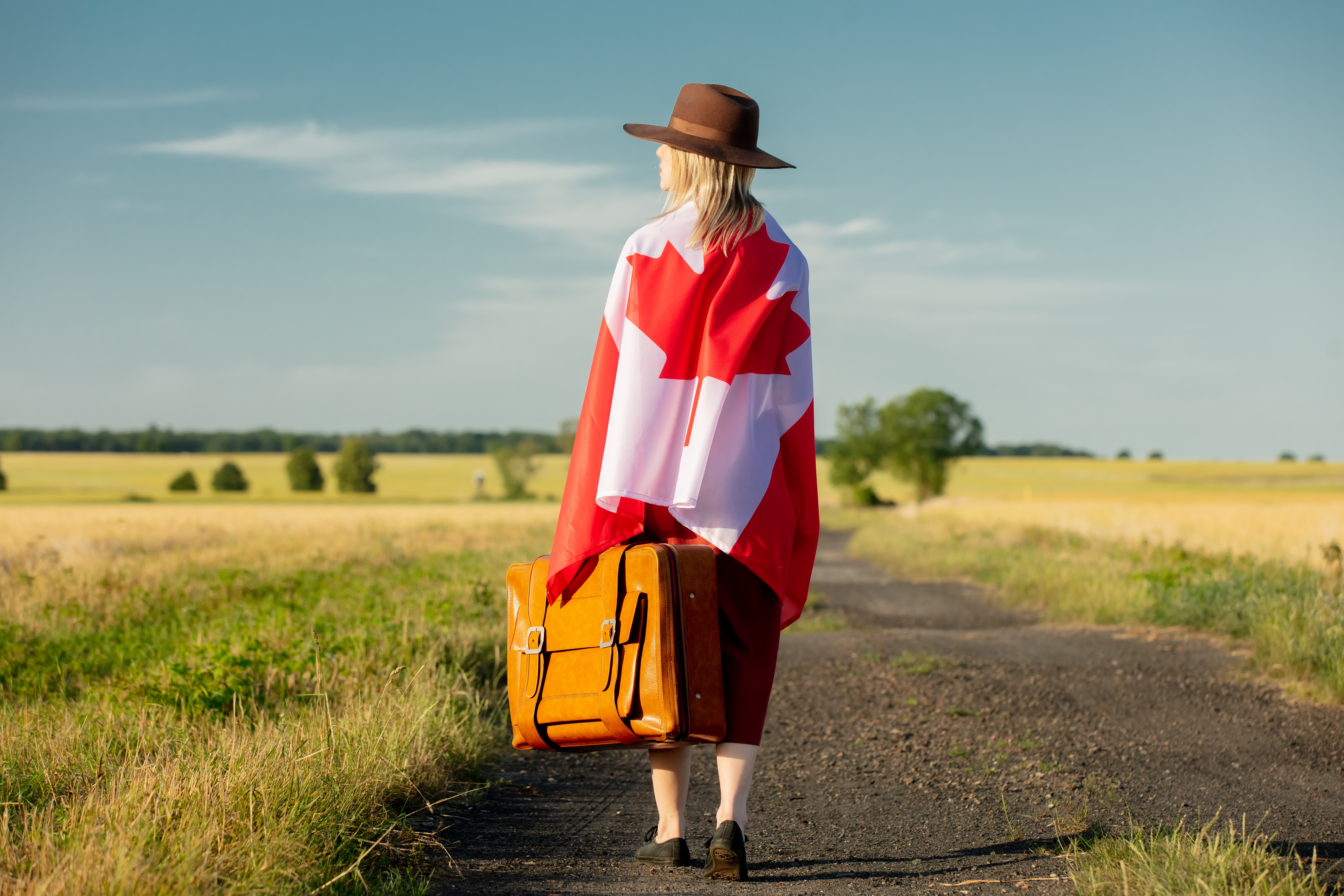 Woman with suitcase wrapped in Canadian flag on country road