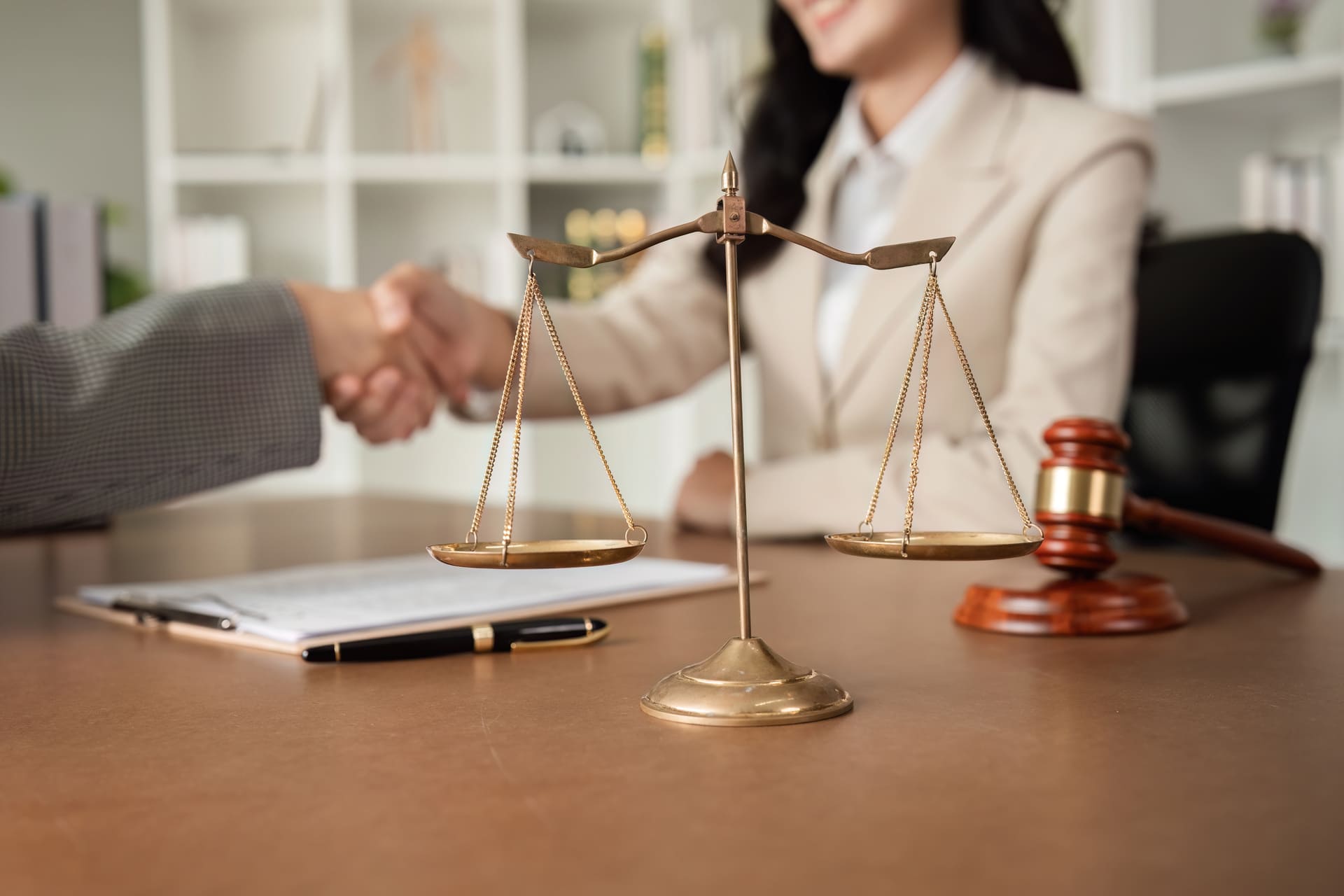 Lawyer and client shaking hands with justice scales and gavel on desk