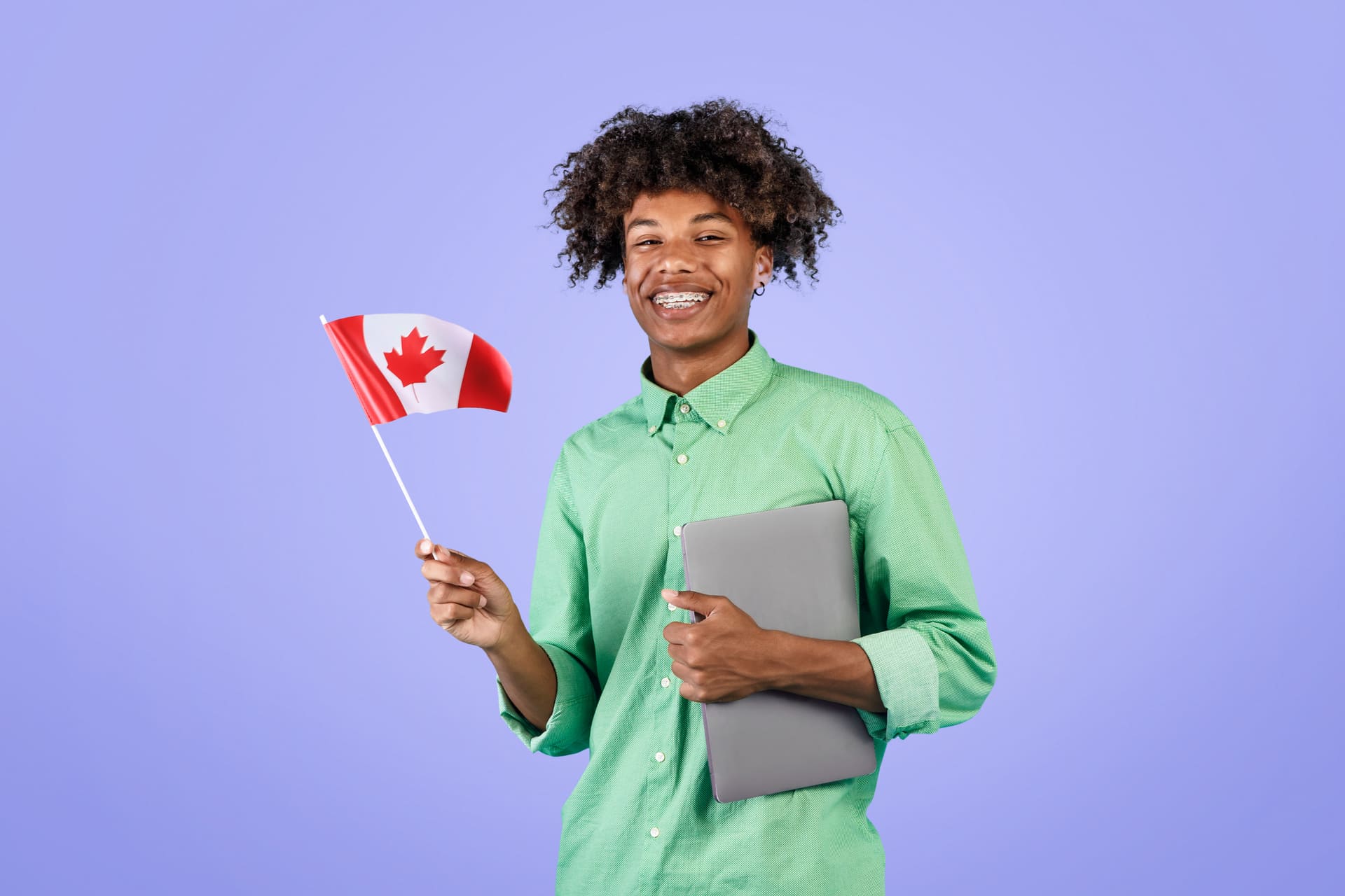 Smiling student holding a Canadian flag and laptop against a purple background